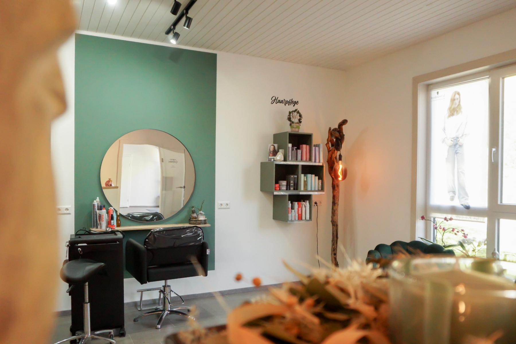 Friseursessel mit Pflegeprodukten an der Wand und großem runden Spiegel auf grüner Wand montiert